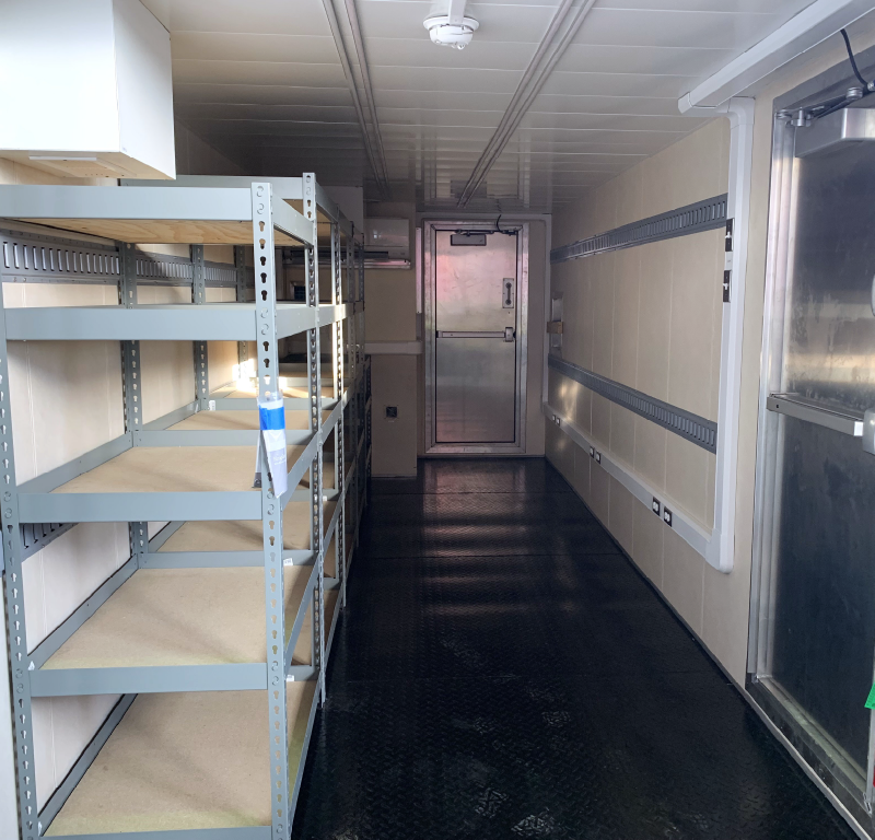 Interior of a modified offshore container with shelving, lighting, electrical service and personnel access door.