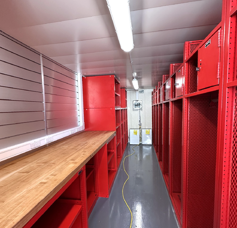 Interior of a modified offshore container configured as a workshop with workbench, storage lockers and electrical outlets.