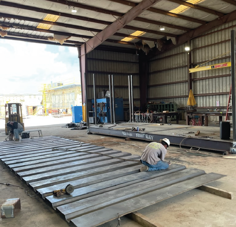 Offshore module fabrication in progress inside a manufacturing facility with steel framing and welding operations.