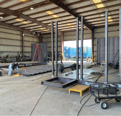 Offshore module fabrication in progress inside a manufacturing facility with steel framing and welding operations.