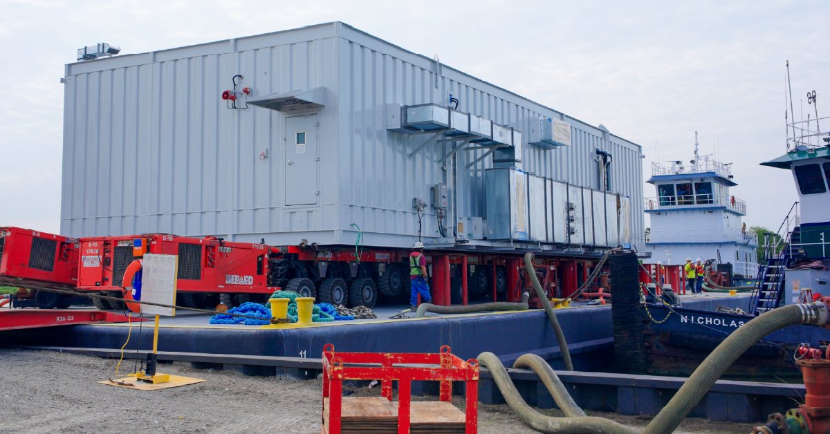 Large prefabricated modular building being transported onto a barge for delivery to an industrial project site.