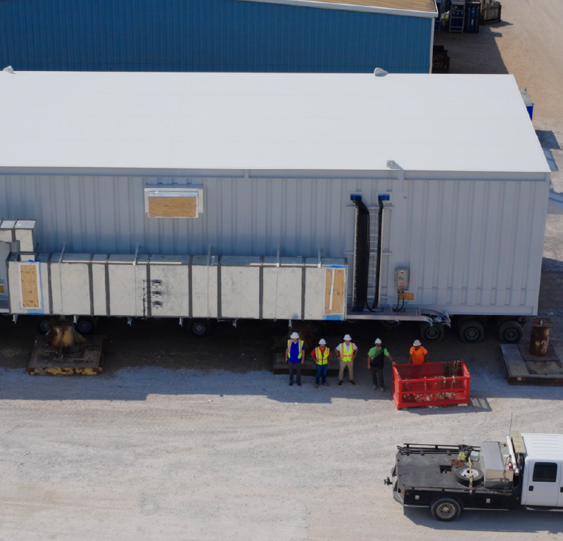 Large prefabricated industrial module at a fabrication yard with workers standing alongside the structure.